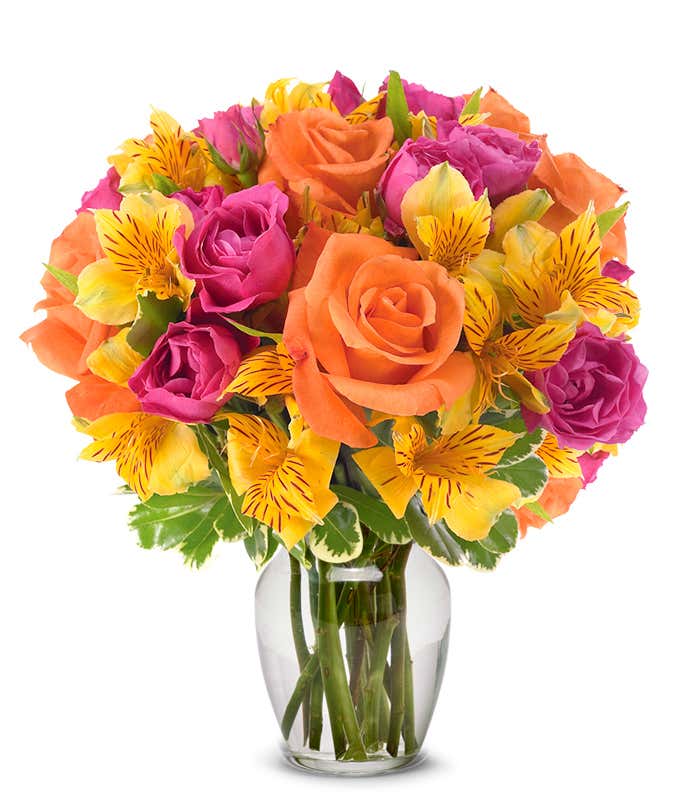 Orange roses, hot pink roses and yellow alstroemeria in glass vase