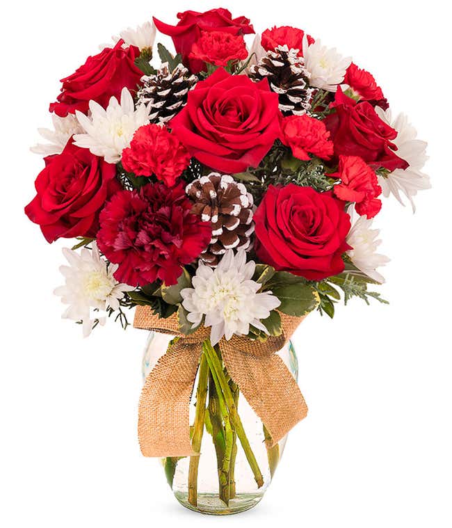 Red roses and carnations arranged with white mums, assorted Christmas greenery, and frosted pinecones, all in a clear vase wrapped with a burlap ribbon.