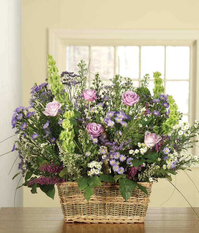 Sympathy arrangement with white roses, purple roses and bells of ireland